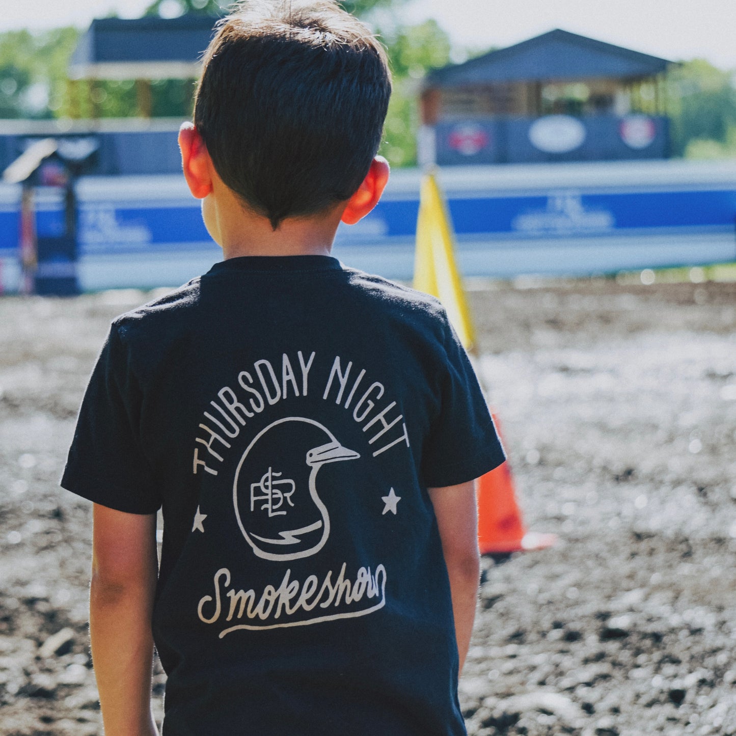 On body image of Youth black short sleeve graphic tees shirt back image of words Thursday Night Smokeshow with a vintage moto helmet with lightning bolt and LSR branding. Shirt is black and graphic is taupe in water based ink.