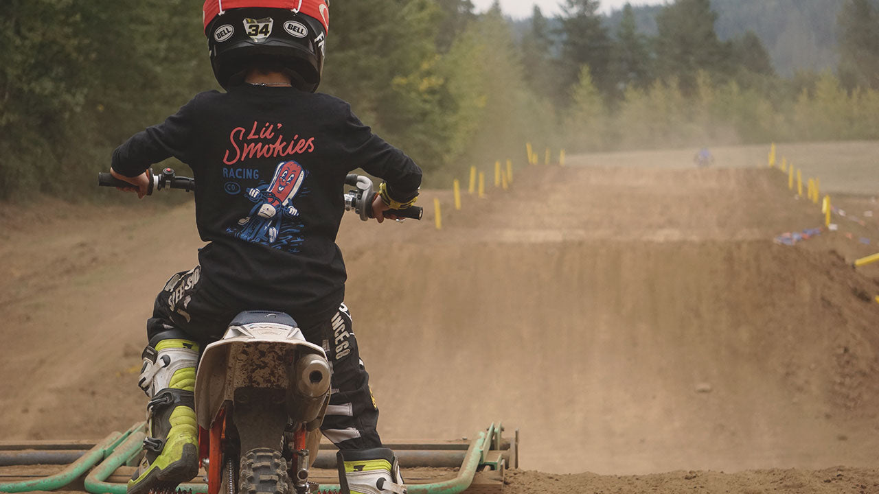 youth dirt bike racer at the starting gate. Featuring Lil' Smokies Racing long sleeved burnt dogs tee in black. Motocross rider on dirtbike. 