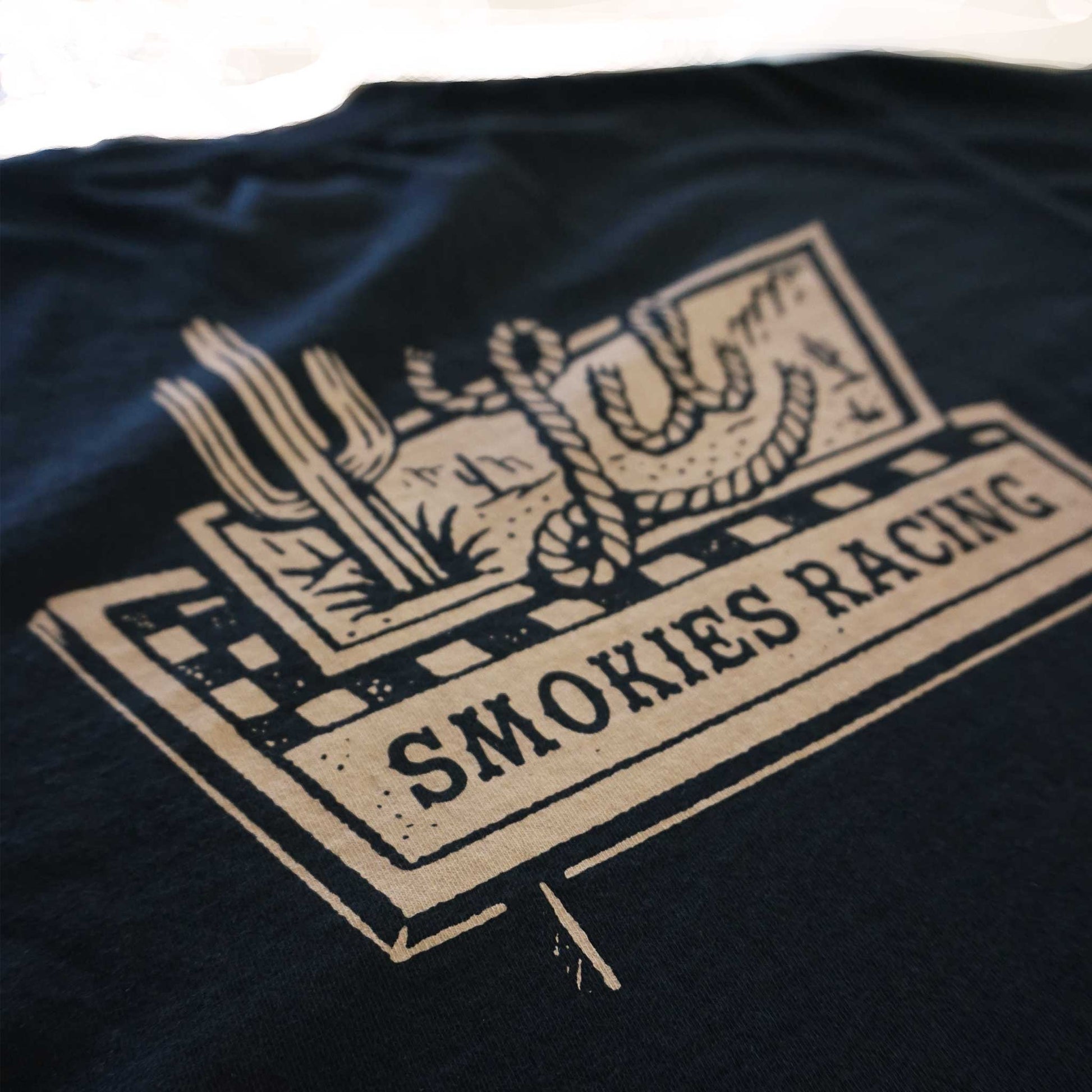 Close product shot of the detail in the design of the road sign tee. Back image the graphic is oversized showing the detail in the sign with a cactus and rope lettering for the word  Lil.