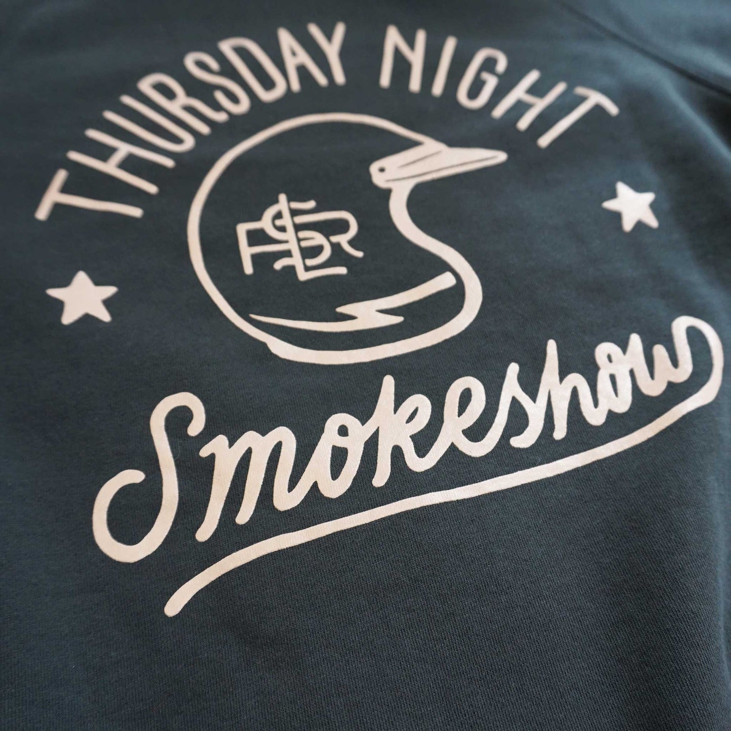 Close up product and logo shot of the back of the crewneck sweatshirt. Thursday Night Smokeshow surrounding a vintage motocross helmet with Lil Smokies racing logo.