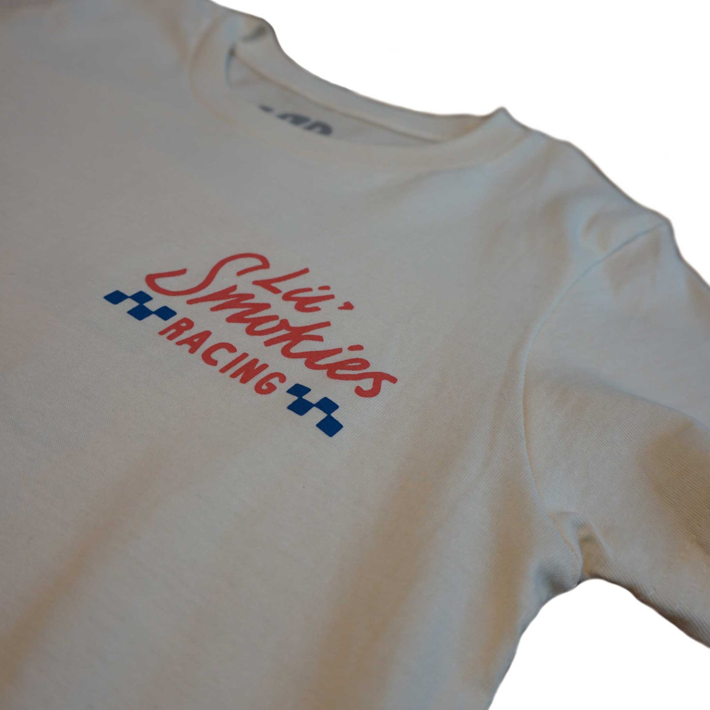 Closeup detailed shot of the ivory short sleeve shirt in youth with the left front chest Lil Smokies Racing branding. Image is printed in a waterbased ink in a faded red and soft blue.