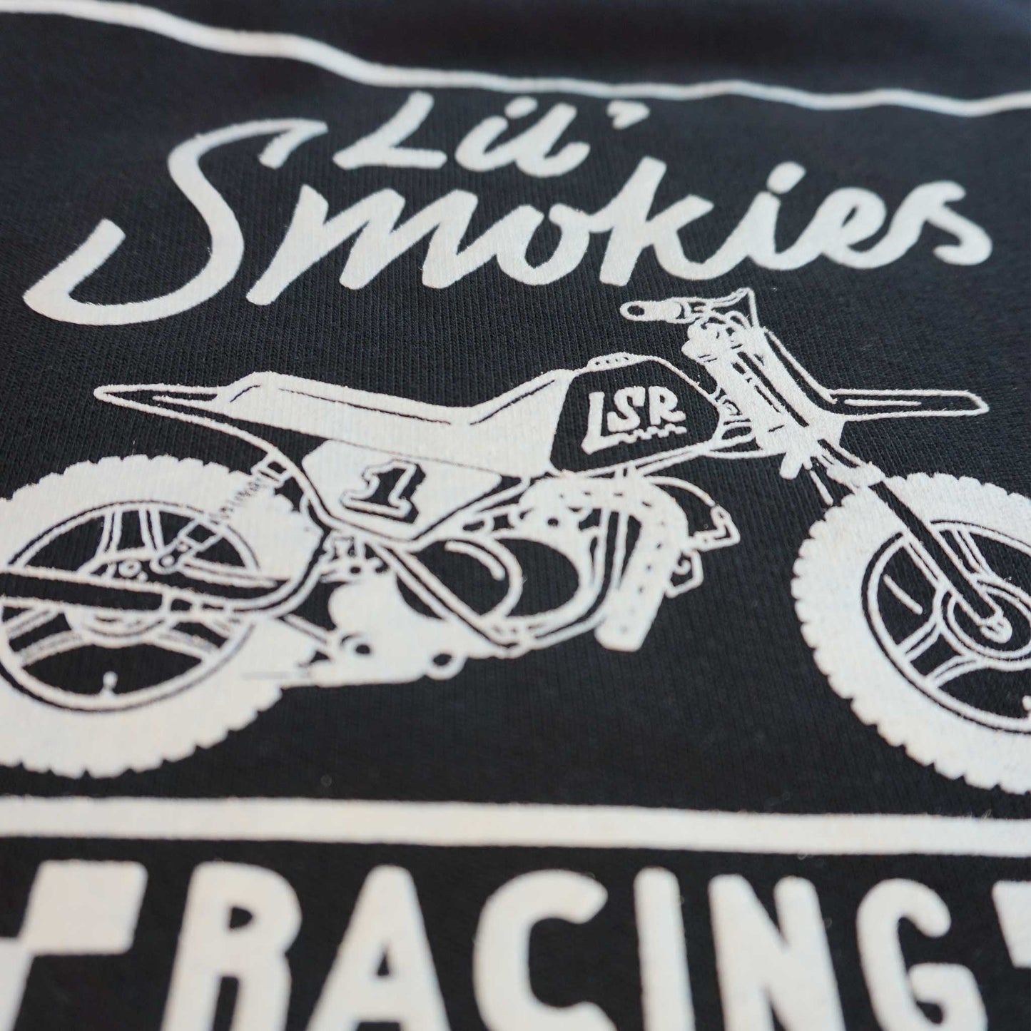 Close up of the youth black long sleeve hoodie featuring the back design of the classic Lil Smokies Racing branding with a dirtbike in white ink. The dirt bike is an original design with LSR graphics and a #1 plate.