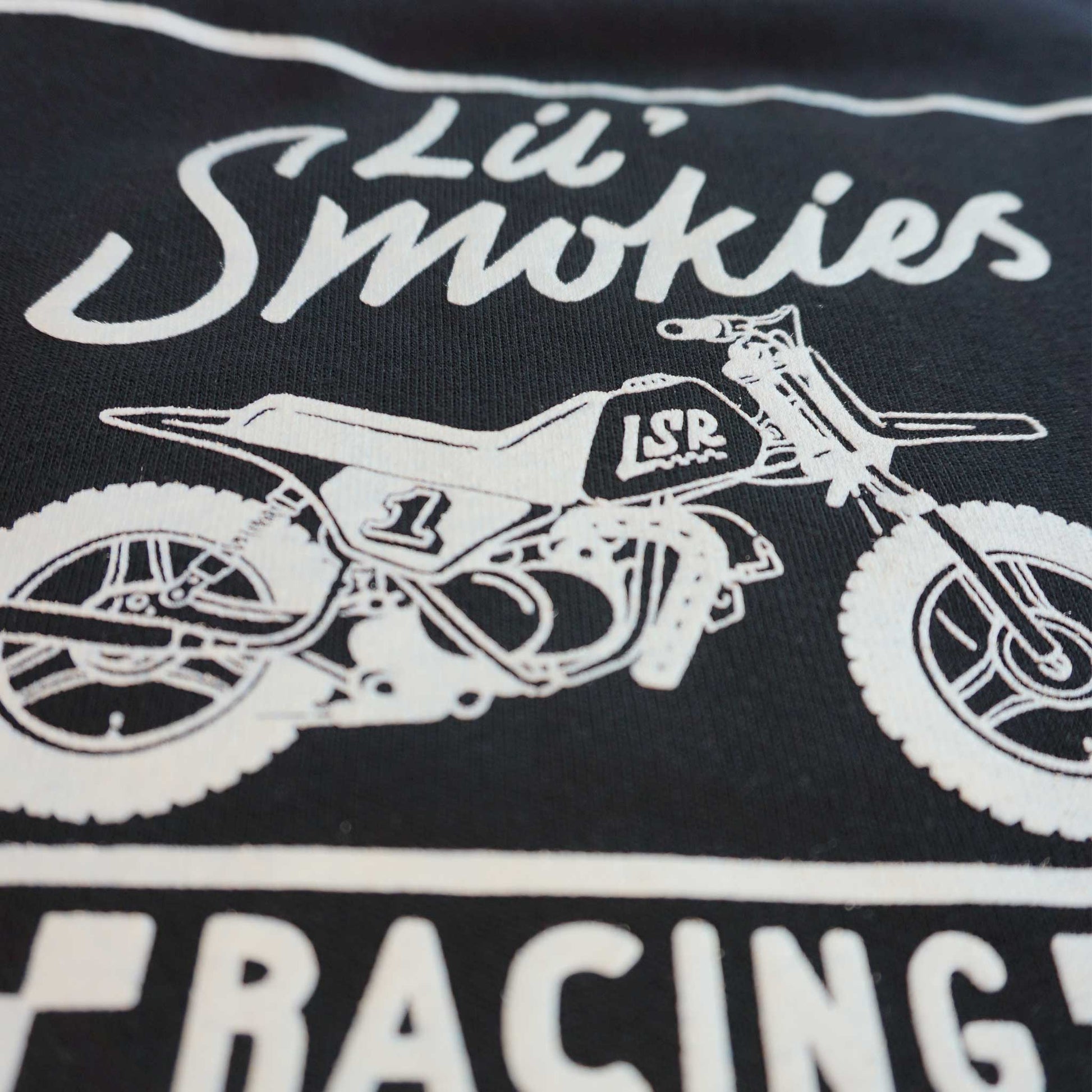 Close up of the youth black long sleeve hoodie featuring the back design of the classic Lil Smokies Racing branding with a dirtbike in white ink. The dirt bike is an original design with LSR graphics and a #1 plate.