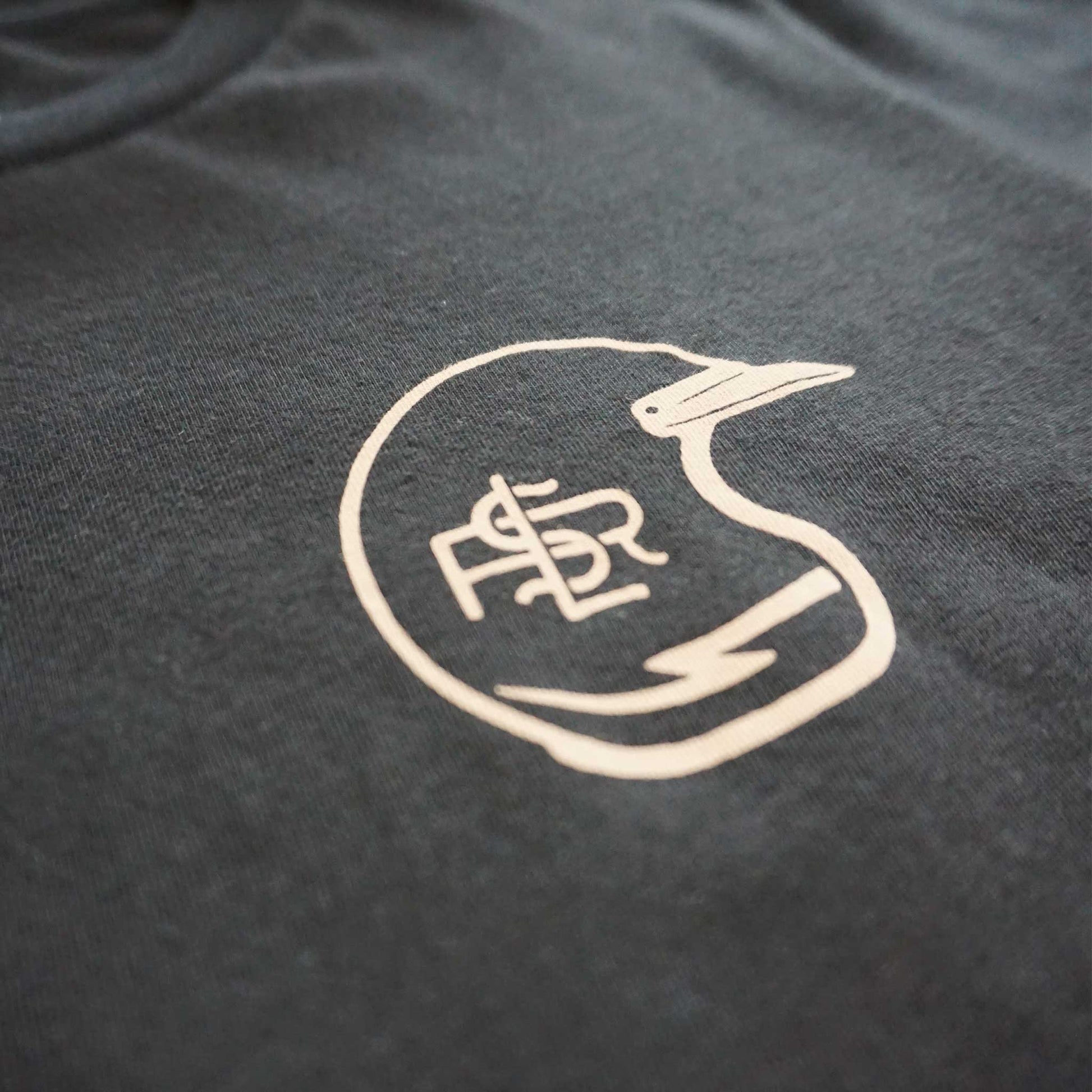 Close up of Front image of the short sleeve black tee with a left front chest graphic of a vintage dirt bike helmet and LSR branding with a lightning bolt. printed in taupe with water based ink.