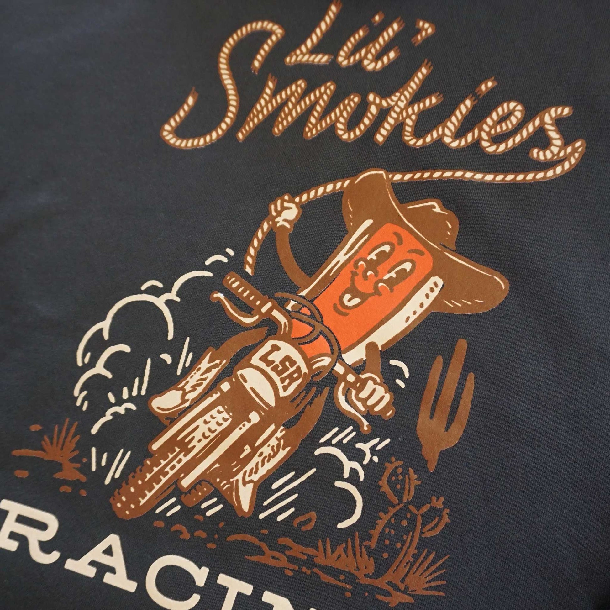 Close up image of the Lil Smokies logo written out in rope lasso with Cowboy Hotdog riding a dirtbike in the dessert